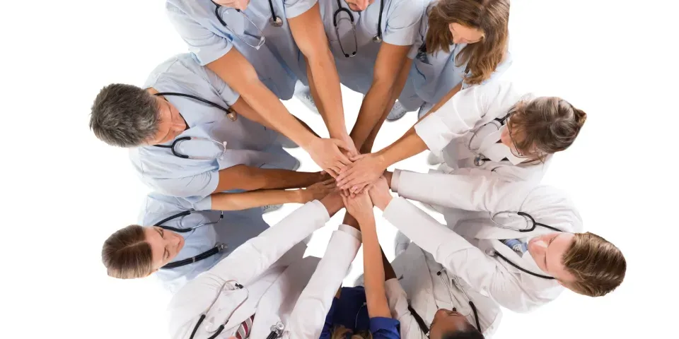 Group of medical professionals in a huddle with their hands stacked in the middle